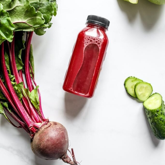 Red Juice in Bottle Beside Beetroot, Apple and Sliced Cucumber